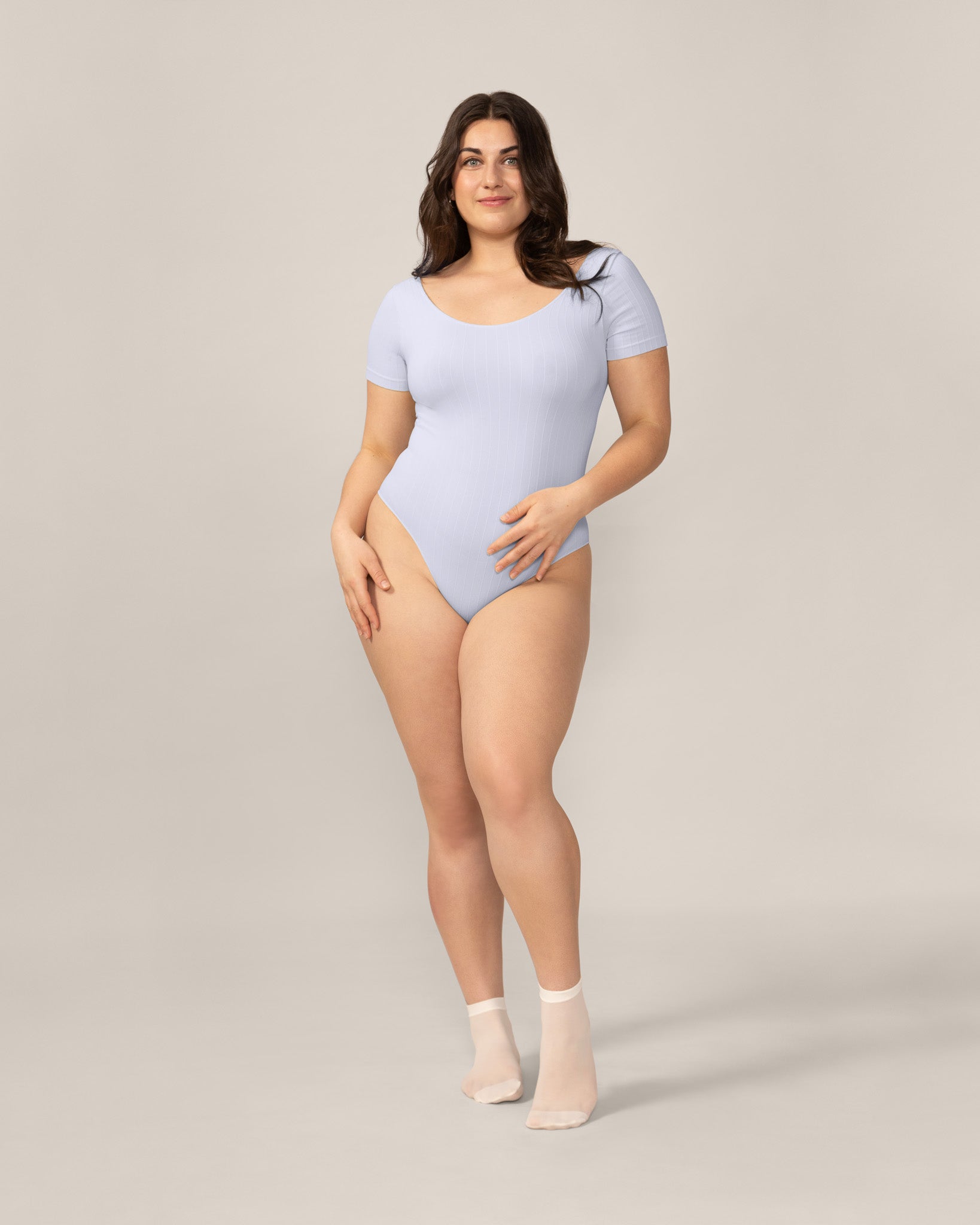 Woman wearing a light blue bodysuit against a plain background