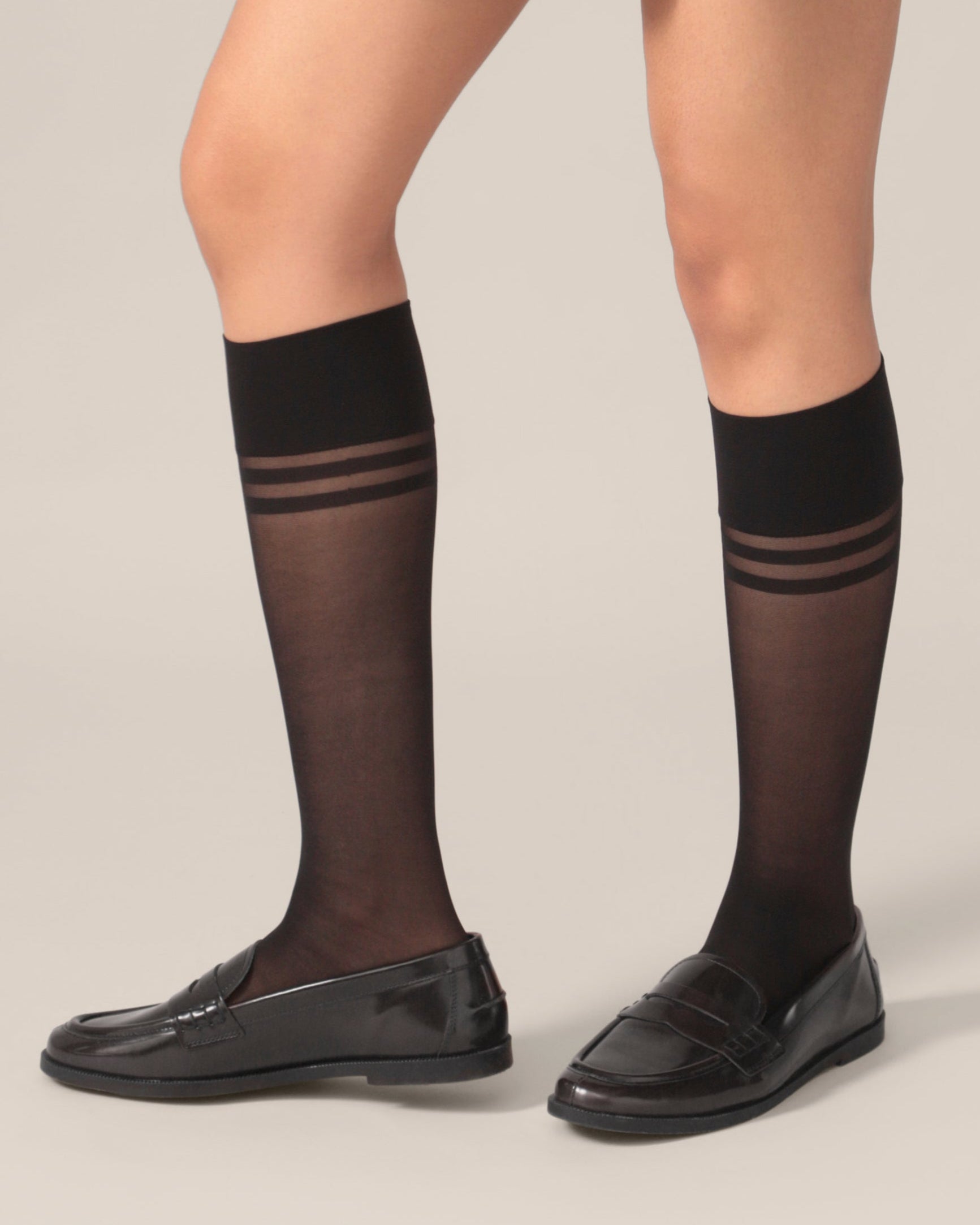 Black knee-high socks with thin stripes worn by a person on a plain background