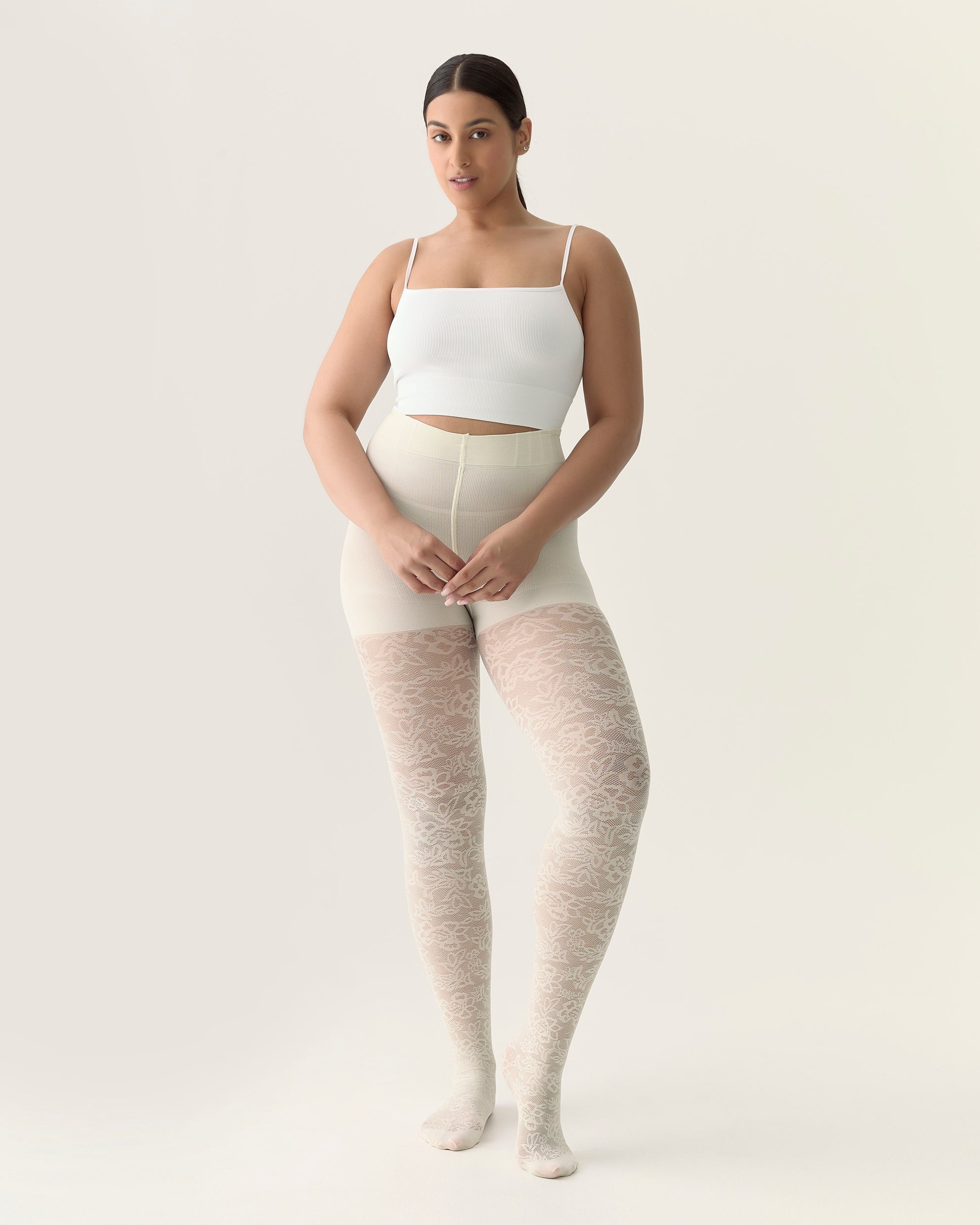 Woman wearing beige tights and a white top on a plain background