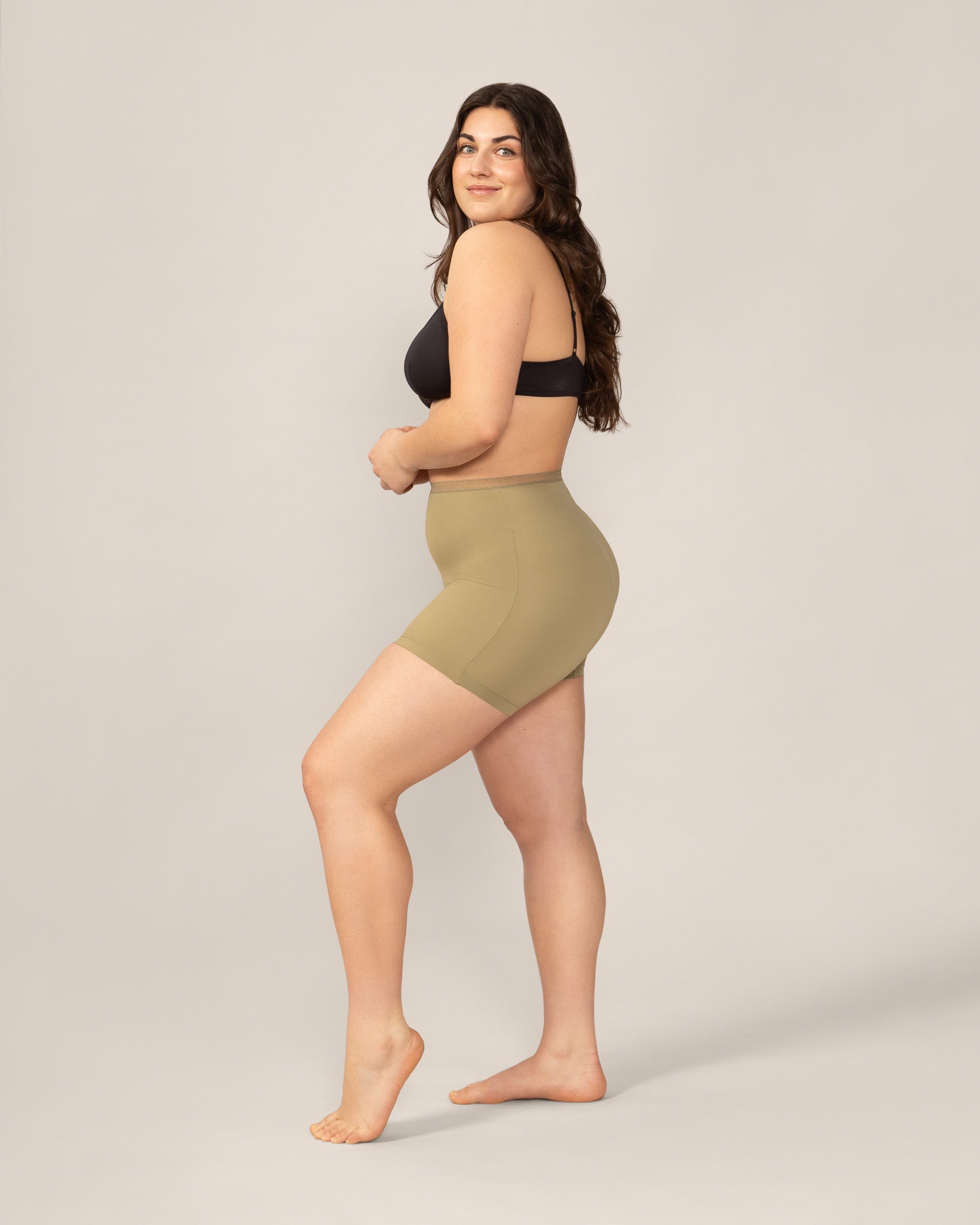 Woman wearing a black bra and green high-waisted anti chaffing shorts on a plain background