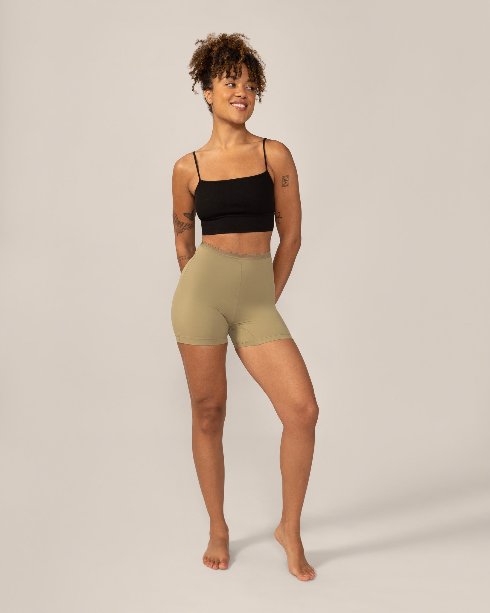 Woman wearing a black crop top and green anti chaffing shorts on a plain background